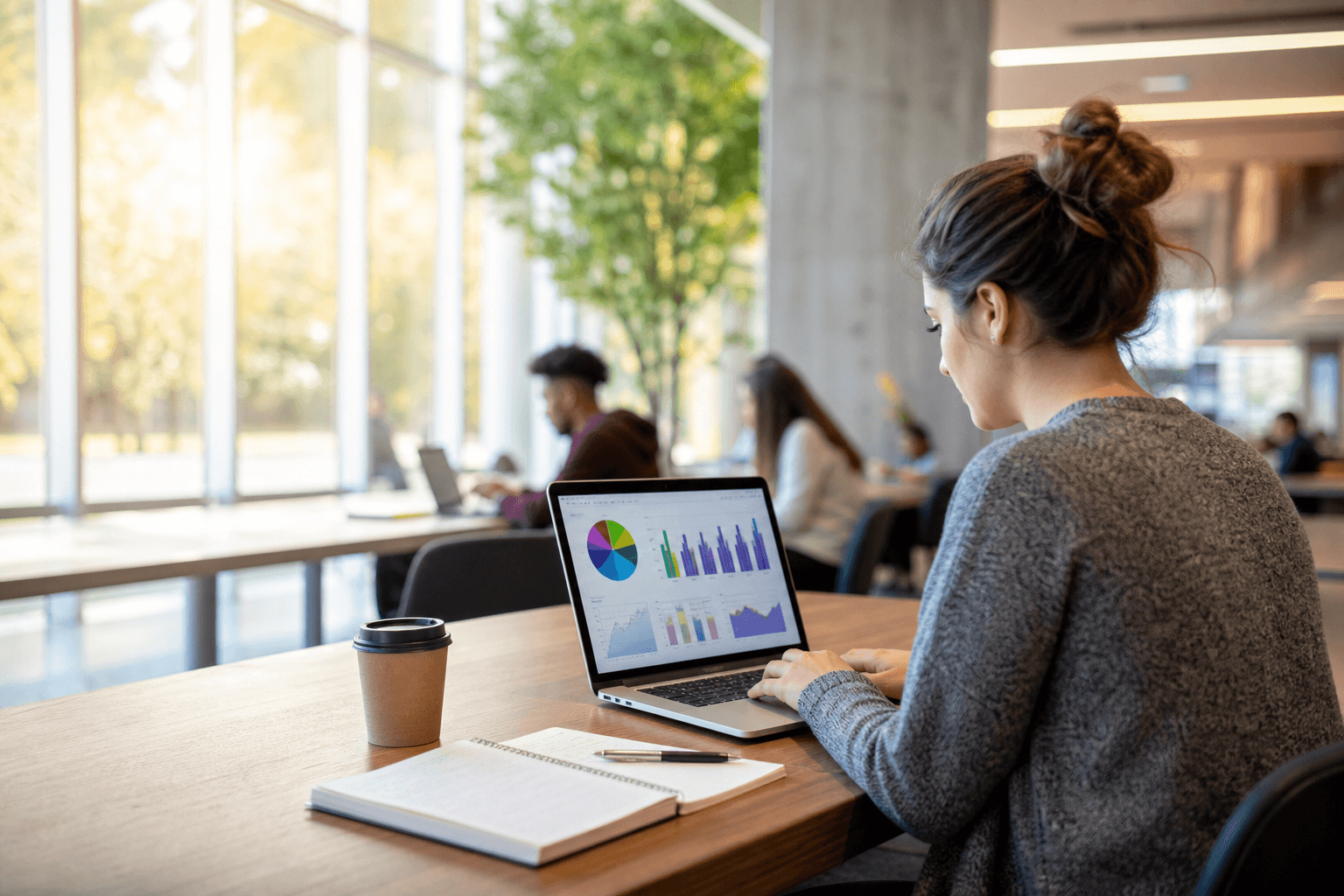 A focused adult student working at a laptop in a bright university study lounge, data charts glowing on the screen.